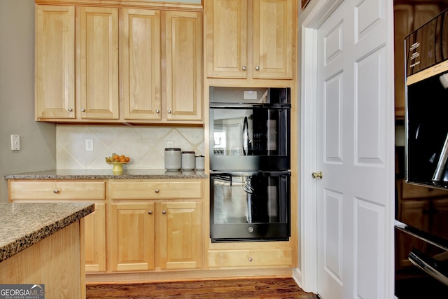 kitchen with black double oven, decorative backsplash, light stone counters, light brown cabinetry, and dark hardwood / wood-style flooring