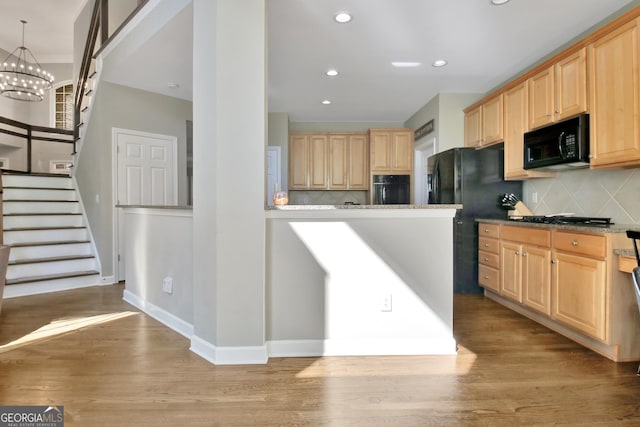 kitchen featuring decorative backsplash, light brown cabinetry, light wood-type flooring, black appliances, and an inviting chandelier