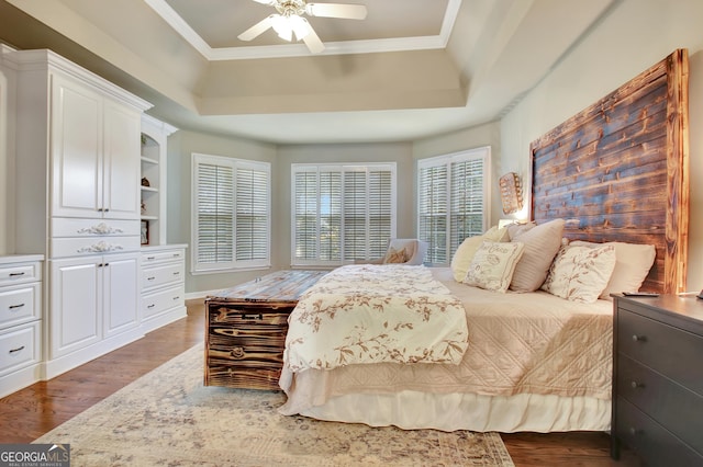 bedroom featuring a tray ceiling, ceiling fan, crown molding, and dark wood-type flooring