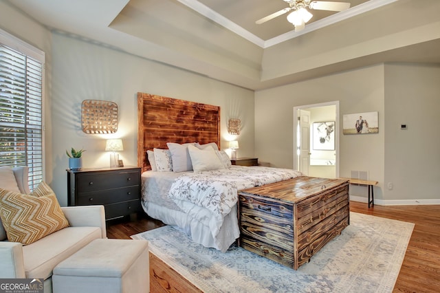 bedroom with dark wood-type flooring, a raised ceiling, ensuite bath, ceiling fan, and ornamental molding