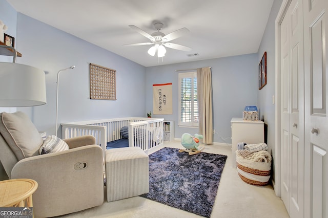 bedroom featuring a nursery area, a closet, ceiling fan, and light colored carpet