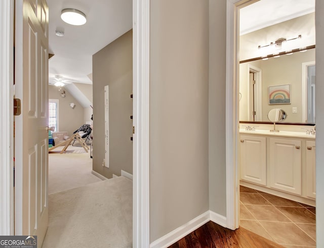 corridor with light colored carpet, sink, and vaulted ceiling