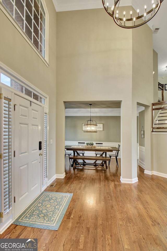 foyer entrance featuring a chandelier, a towering ceiling, light wood-type flooring, and crown molding