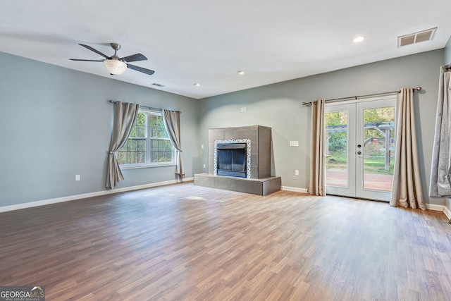 unfurnished living room with french doors, a tiled fireplace, ceiling fan, and hardwood / wood-style floors