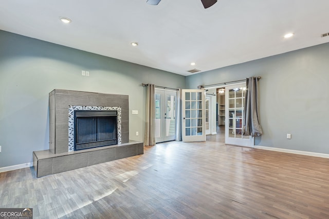 unfurnished living room with french doors, a tiled fireplace, hardwood / wood-style floors, and ceiling fan