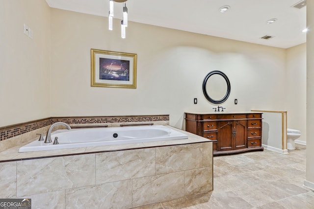 bathroom featuring tiled bath, vanity, and toilet