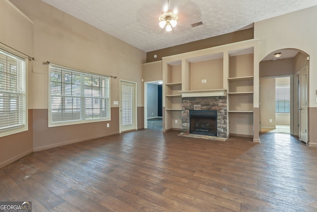 unfurnished living room featuring a fireplace, a textured ceiling, ceiling fan, built in features, and dark hardwood / wood-style flooring