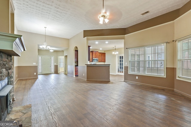 unfurnished living room with a textured ceiling, dark wood-type flooring, a stone fireplace, and ceiling fan with notable chandelier