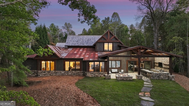 back house at dusk featuring a patio area, a lawn, and a fire pit