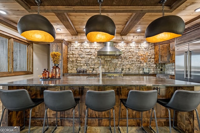 kitchen with wood ceiling, wall chimney exhaust hood, beamed ceiling, a kitchen bar, and stainless steel built in refrigerator