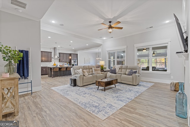 living room with light wood finished floors, ornamental molding, visible vents, and a ceiling fan