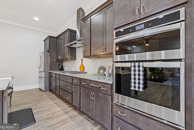 kitchen with crown molding, backsplash, appliances with stainless steel finishes, dark brown cabinets, and wall chimney exhaust hood