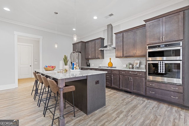 kitchen with a breakfast bar, tasteful backsplash, appliances with stainless steel finishes, a kitchen island with sink, and wall chimney exhaust hood