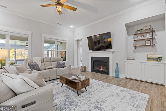 living room featuring light wood-type flooring, visible vents, crown molding, and a glass covered fireplace