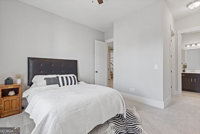 bedroom with ensuite bathroom, light carpet, a sink, a ceiling fan, and baseboards