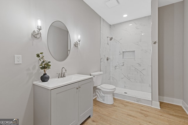 full bathroom featuring toilet, vanity, wood finished floors, tiled shower, and baseboards