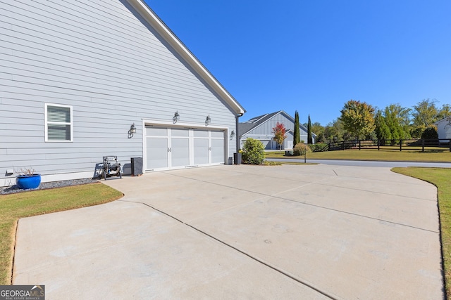 view of side of home featuring a garage, concrete driveway, a lawn, and fence