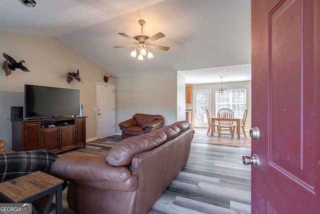 living room featuring lofted ceiling, ceiling fan with notable chandelier, and light hardwood / wood-style floors