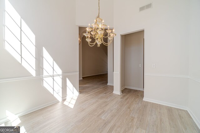 unfurnished dining area with a chandelier, a towering ceiling, and light hardwood / wood-style flooring