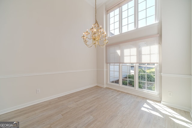 empty room with a chandelier, light wood-type flooring, a wealth of natural light, and a towering ceiling