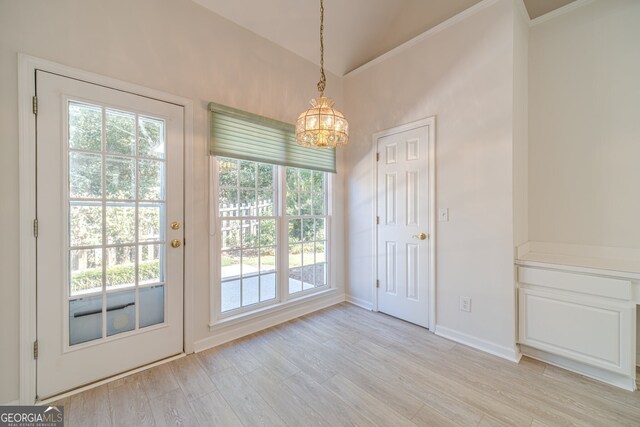 entryway with an inviting chandelier, light wood-type flooring, vaulted ceiling, and ornamental molding