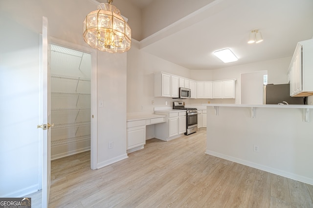 kitchen with white cabinets, light hardwood / wood-style floors, decorative light fixtures, and appliances with stainless steel finishes