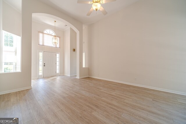 entryway with a towering ceiling, light wood-type flooring, ceiling fan, and crown molding