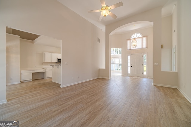 unfurnished living room with ceiling fan with notable chandelier, light hardwood / wood-style floors, and a towering ceiling