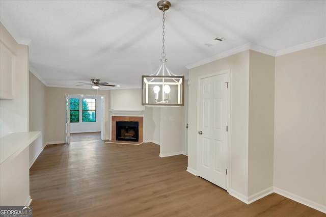 unfurnished living room featuring crown molding, wood-type flooring, a tile fireplace, and ceiling fan