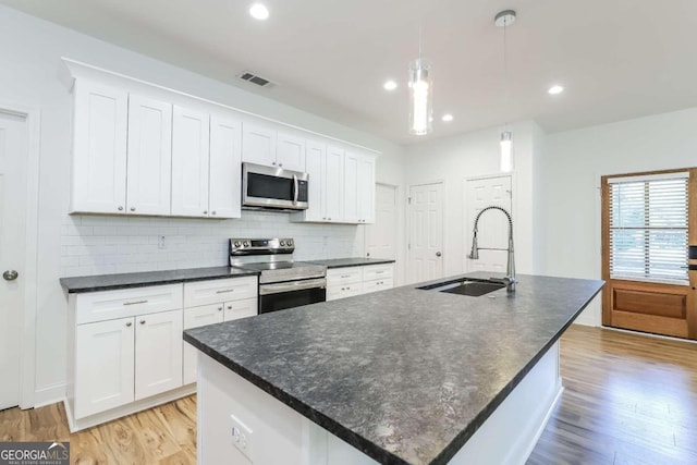 kitchen featuring a center island with sink, sink, appliances with stainless steel finishes, and hanging light fixtures