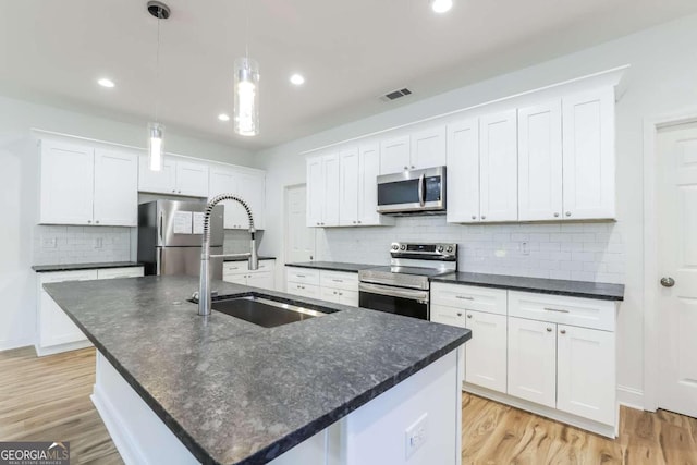 kitchen featuring appliances with stainless steel finishes, sink, an island with sink, decorative light fixtures, and white cabinets