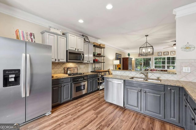 kitchen with wood-type flooring, sink, ornamental molding, appliances with stainless steel finishes, and decorative light fixtures