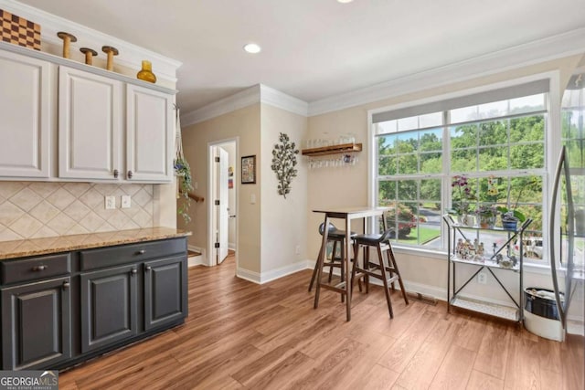 kitchen featuring hardwood / wood-style flooring, tasteful backsplash, ornamental molding, light stone countertops, and white cabinets