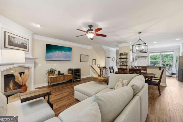 living room featuring ceiling fan with notable chandelier, hardwood / wood-style flooring, and crown molding