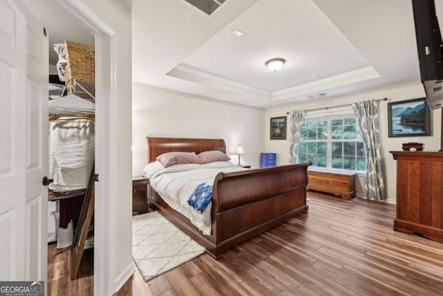 bedroom featuring a tray ceiling, wood-type flooring, and ornamental molding