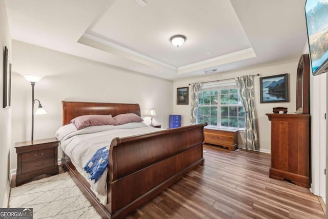 bedroom with hardwood / wood-style floors, ornamental molding, and a tray ceiling