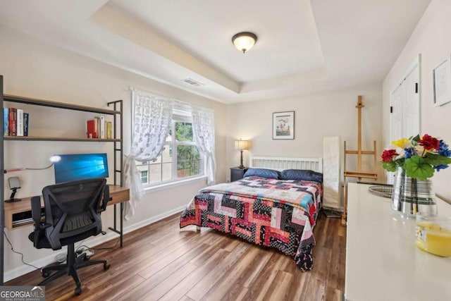 bedroom with dark wood-type flooring and a tray ceiling