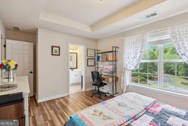 bedroom with a tray ceiling, light hardwood / wood-style floors, and ensuite bath