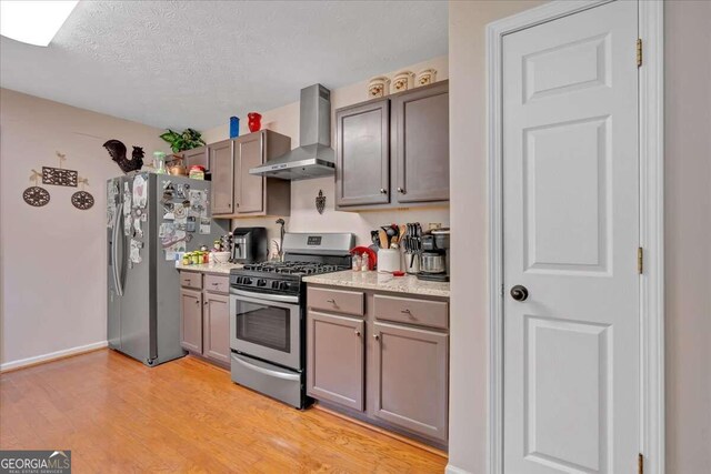 kitchen with appliances with stainless steel finishes, a textured ceiling, wall chimney range hood, and light hardwood / wood-style floors