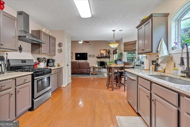 kitchen with wall chimney range hood, stainless steel appliances, sink, a textured ceiling, and light hardwood / wood-style floors