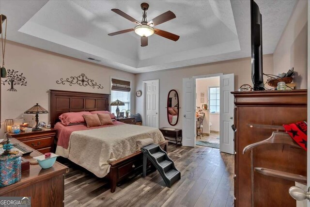 bedroom featuring ceiling fan, wood-type flooring, a tray ceiling, and ensuite bathroom