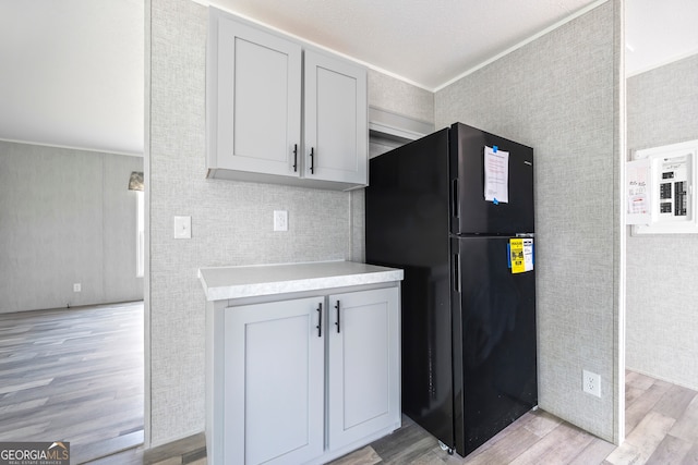 kitchen with black refrigerator, crown molding, light hardwood / wood-style flooring, and electric panel