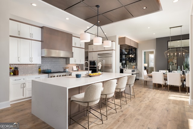 kitchen with a center island with sink, built in appliances, light hardwood / wood-style flooring, and white cabinetry