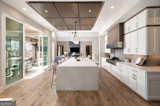 kitchen featuring white cabinetry, wall chimney range hood, an island with sink, and hardwood / wood-style floors