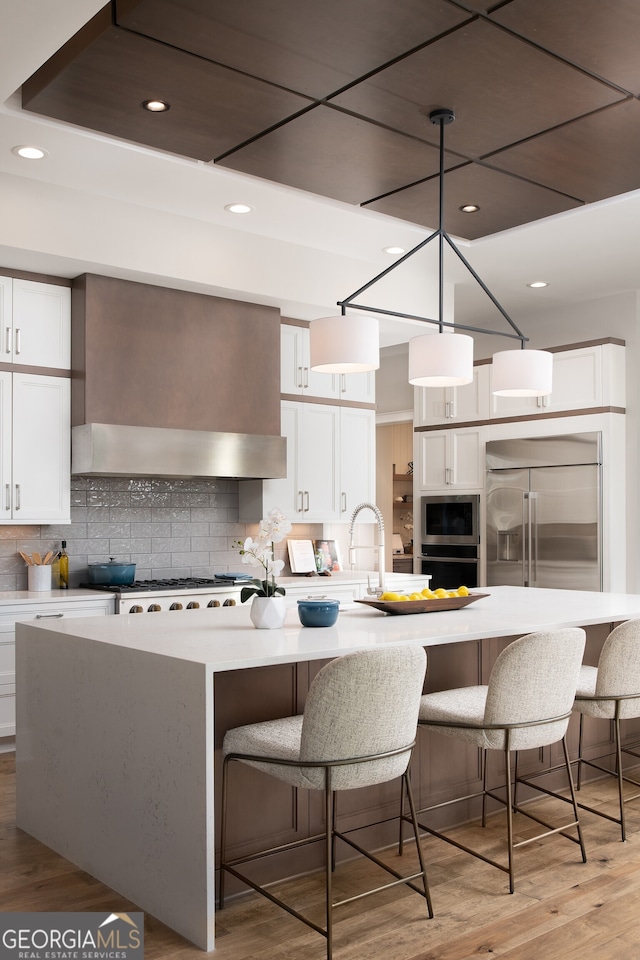 kitchen featuring white cabinets, a spacious island, light hardwood / wood-style floors, decorative light fixtures, and stainless steel appliances