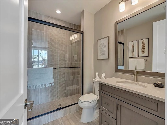 bathroom with a shower with door, vanity, hardwood / wood-style flooring, and toilet