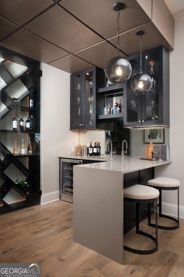 bar featuring sink, decorative light fixtures, wood-type flooring, and beverage cooler