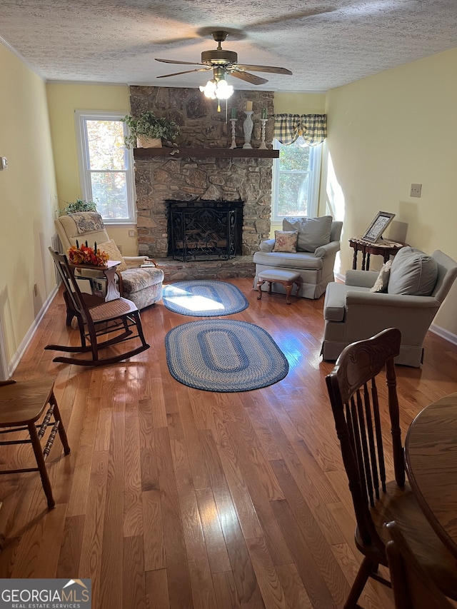 living room with ceiling fan, a stone fireplace, a textured ceiling, and wood-type flooring