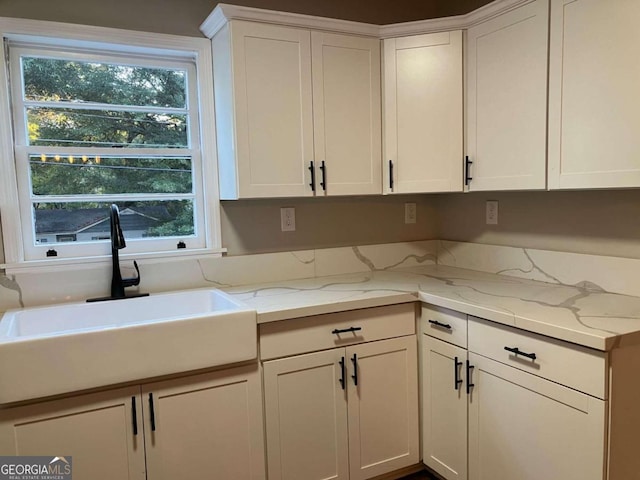 kitchen featuring a healthy amount of sunlight, light stone countertops, sink, and white cabinets