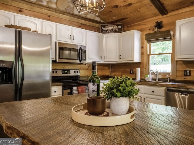 kitchen with wood walls, sink, vaulted ceiling, white cabinetry, and stainless steel appliances